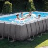 Large Intex rectangular metal-frame pool with clear blue water, accompanied by a white safety ladder and sand filter pump system.